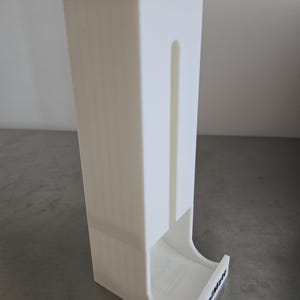 May include: A white, rectangular dispenser with a curved base and a vertical slot. The text "SpoolMate" is printed in black on the base. The dispenser is made of a solid, opaque material.