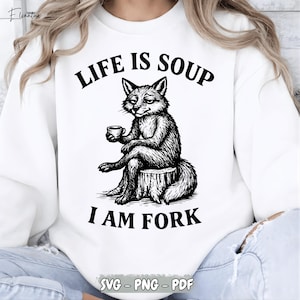 Puede incluir: Sudadera blanca con una ilustración en blanco y negro de un zorro sentado en un tocón de árbol, sosteniendo una taza. El texto "LIFE IS SOUP I AM FORK" está impreso encima y debajo del zorro. La parte inferior de la sudadera tiene el texto "SVG - PNG - PDF".