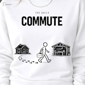 May include: White sweatshirt with a black and white graphic. The graphic depicts a stick figure walking from a house to a workshop, with the words "THE DAILY COMMUTE" above. The design includes a house, footprints, and a workshop.