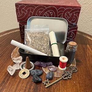 May include: A red wooden box with a Celtic knot design, a black tin, and various items for spiritual practices. Includes a bag of herbs, crystals, a scroll, a small bottle, a spool of red thread, a key, and a coin.