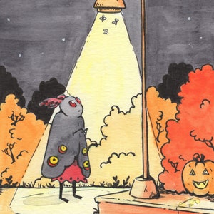 May include: A black and red moth with large eyes stands under a streetlight in a park at night. The streetlight is casting a yellow glow on the moth and the surrounding trees. There is a jack-o'-lantern on the ground to the right of the moth.