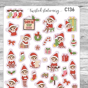 May include: A sticker sheet featuring various Christmas-themed illustrations. The stickers include elves, stockings, gifts, candy canes, and a sign that reads "Santa Stop Here." The sheet also includes the text "Twisted Stationery" and the code "C136".