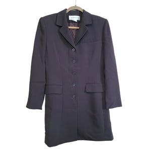 May include: A long, dark purple blazer with a notched collar, six buttons, and two front pockets. The blazer is hanging on a wooden hanger. The lining is a darker shade of purple.