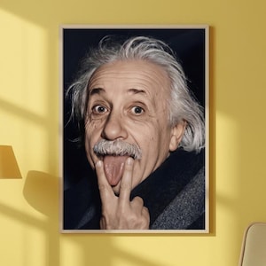 May include: Framed portrait of Albert Einstein sticking out his tongue and making a hand gesture. The image features a close-up of Einstein's face, with his white hair and mustache. The portrait is in a wooden frame.
