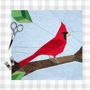 May include: A red cardinal bird perched on a brown branch with green leaves. The bird is made of fabric and is part of a patchwork quilt.