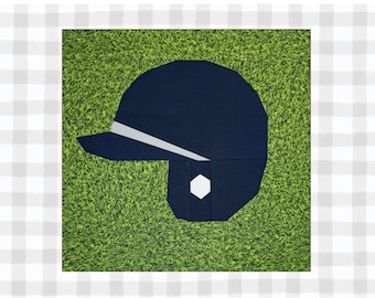 May include: A blue baseball helmet with a white brim and a white circle on the side, set against a green grassy background.