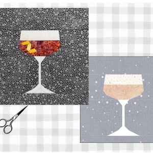 May include: A fabric art piece featuring a cocktail glass design. The glass has a white stem and a red and brown drink with a yellow garnish. The background is a speckled gray pattern. A smaller image of a similar glass is also present.
