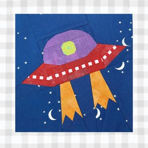 May include: A colorful fabric art piece featuring a red and purple UFO with orange exhaust flames against a dark blue starry sky. White stars and crescent moons are scattered around the spacecraft.