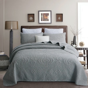 May include: A gray quilted bedspread with a damask pattern. The bedspread is on a bed with white pillows and a brown headboard. There are three framed pictures on the wall behind the bed.