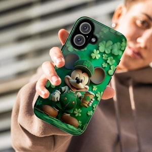 May include: A green phone case with a cartoon image of Mickey Mouse dressed in a green leprechaun costume holding a green beer mug. The case has a shamrock design and the words "Happy St. Patrick's Day" are printed on the case.