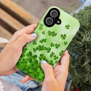 May include: A green phone case with a pattern of four-leaf clovers and glitter. The case has a black camera lens with two circles.