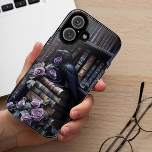 May include: A black raven perched on a stack of old books with purple roses. The phone case features a dark, gothic aesthetic.