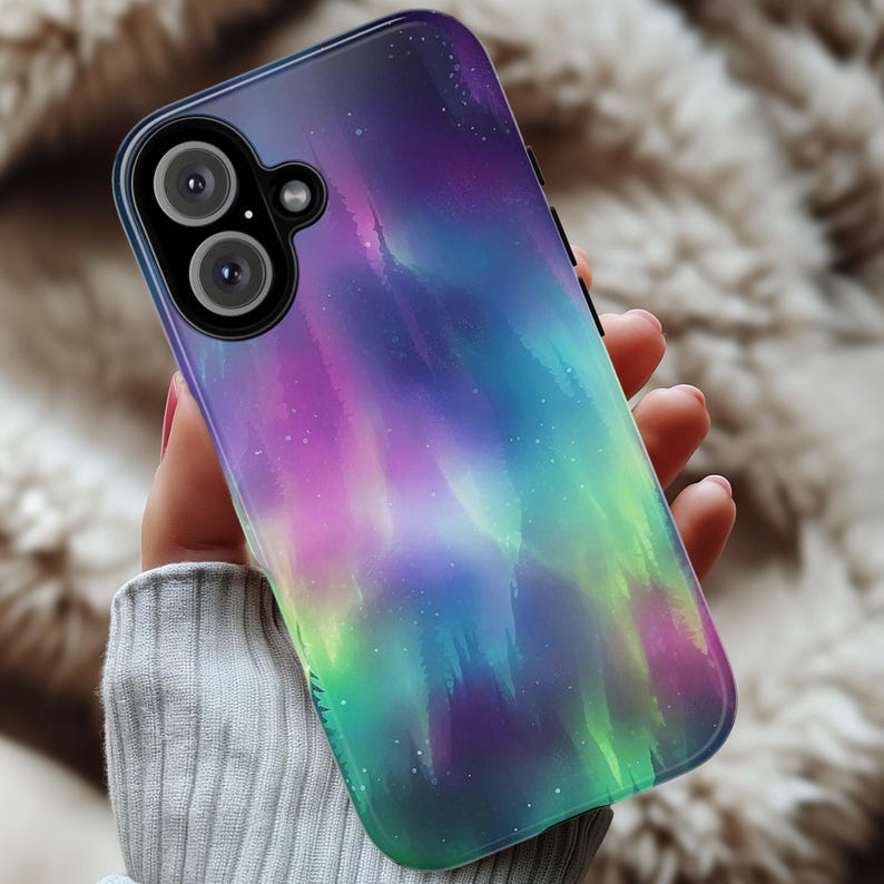 Puede incluir: Una funda de tel&eacute;fono negra con un dise&ntilde;o de aurora boreal colorido. La funda presenta una aurora p&uacute;rpura, verde y azul con un fondo de cielo estrellado.