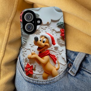 May include: A phone case with a cartoon dog wearing a Santa hat and red scarf. The case has a 3D design with white, red, and yellow accents, and is decorated with snowflakes and poinsettias. The phone case is in a denim pocket.