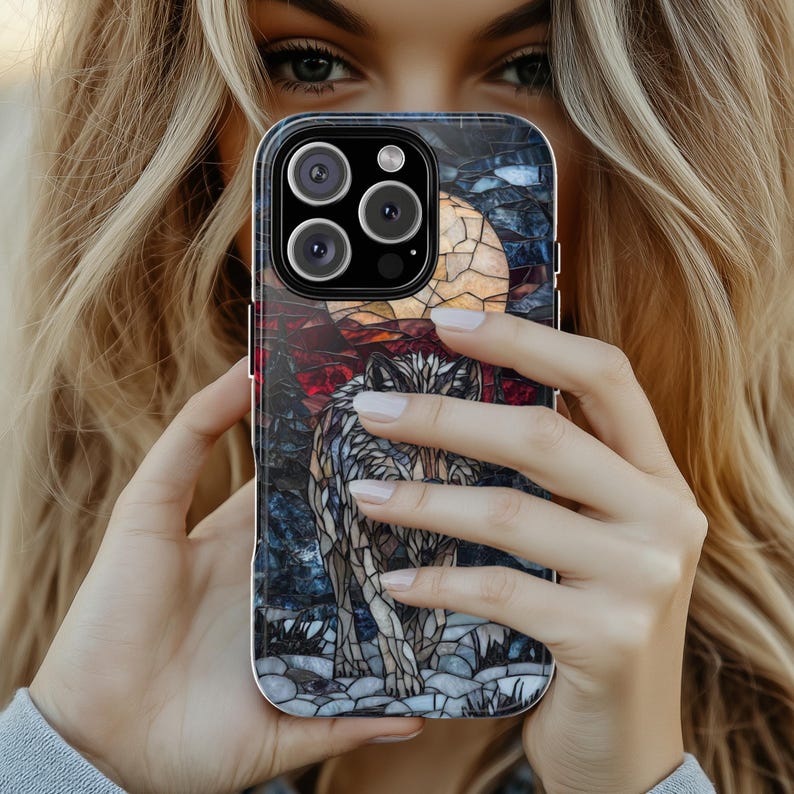 May include: A smartphone case featuring a stained-glass design of a wolf under a full moon. The case has a dark background with red, blue, and yellow accents. The wolf is depicted in shades of gray and white.