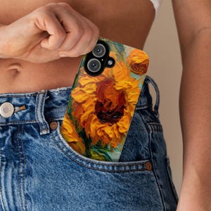 May include: A phone case with a vibrant sunflower painting design. The case has a clear back and a black frame. The sunflower is painted in a thick, textured style, with yellow petals and a dark brown center.