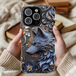 May include: A black phone case with a detailed design of a wolf's head in blue and gold. The wolf's head is surrounded by intricate floral patterns.
