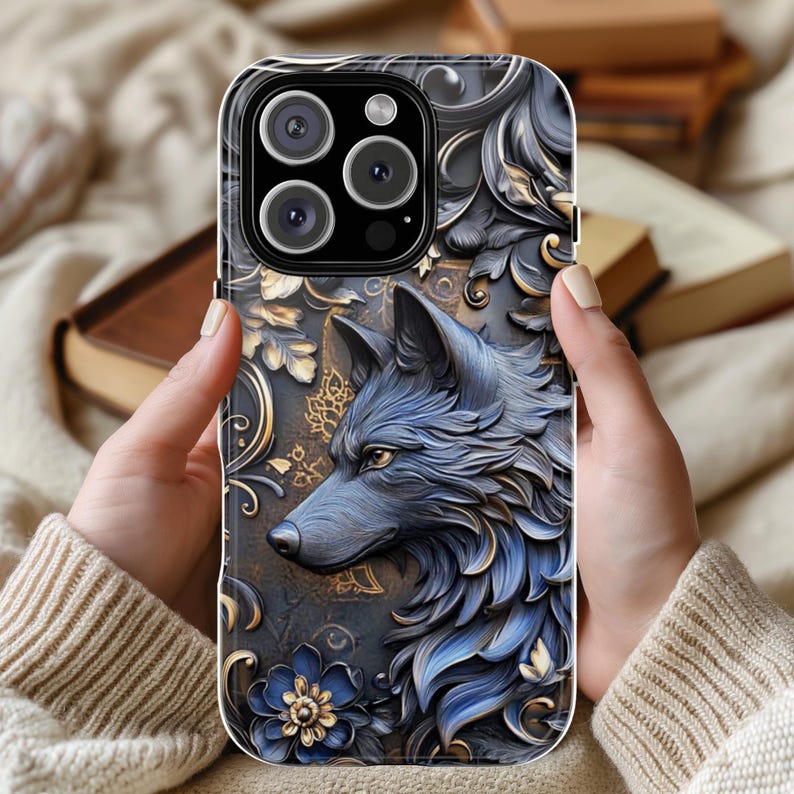 May include: A black phone case with a detailed design of a wolf's head in blue and gold. The wolf's head is surrounded by intricate floral patterns.