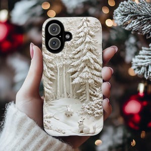May include: White phone case featuring a winter forest scene. The case has a 3D design of snow-covered trees and two small white rabbits.