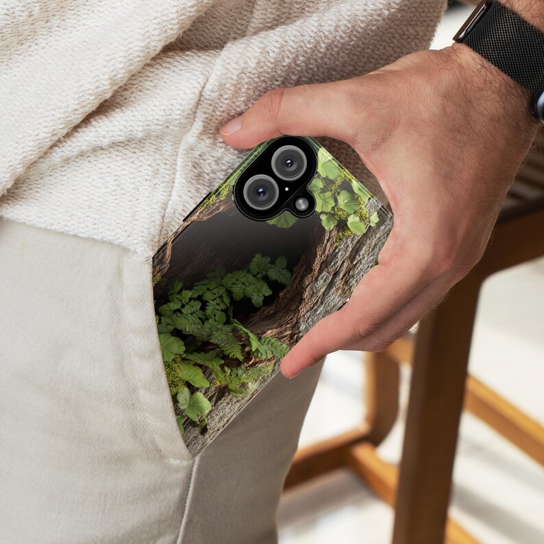May include: A phone case with a nature-inspired design featuring a close-up of a tree trunk with green foliage and a hollow space. The case has a black background and a clear, protective layer over the design.