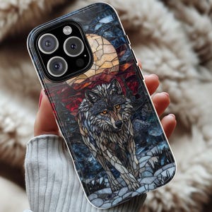 May include: A smartphone case featuring a mosaic-style illustration of a wolf under a full moon. The design incorporates shades of gray, brown, red, and blue. The wolf has yellow eyes and is set against a night sky.