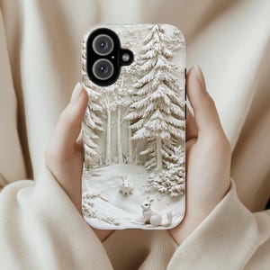 May include: A white phone case featuring a 3D design of a snowy woodland scene with two white rabbits. The case has a black camera lens cutout.