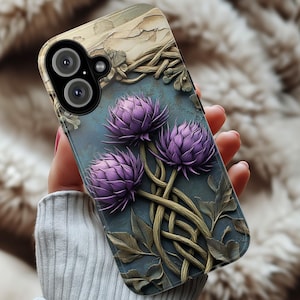 Może przedstawiać: Etui na telefon z szczegółowym kwiatowym wzorem. Etui ma teksturowane, niebiesko-zielone tło z trzema fioletowymi kwiatami ostu i przeplatanymi łodygami. Górna część etui ma teksturowany, przypominający korę wzór.