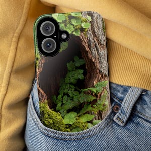 May include: A clear phone case with a design of a tree trunk, green leaves, and moss. The case is in a blue jean pocket.