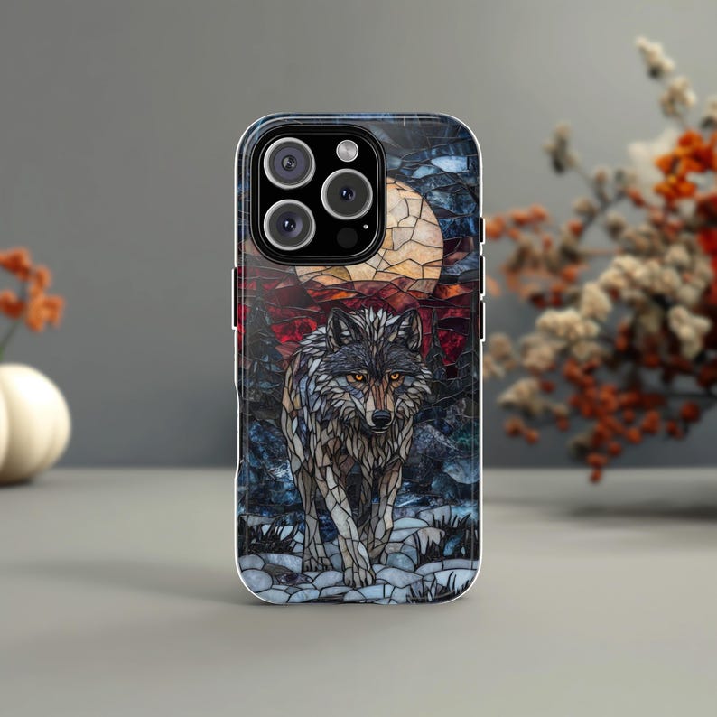 May include: A phone case featuring a mosaic-style image of a wolf under a full moon. The design incorporates shades of gray, brown, and blue, with the wolf's eyes highlighted in orange. The case has a glossy finish and a camera module.