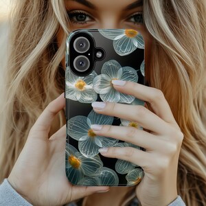 Op de afbeelding: Een transparante telefoonhoes met een bloemenontwerp met witte bloemen op een zwarte achtergrond. De hoes heeft een verhoogde camerabult met twee lenzen.