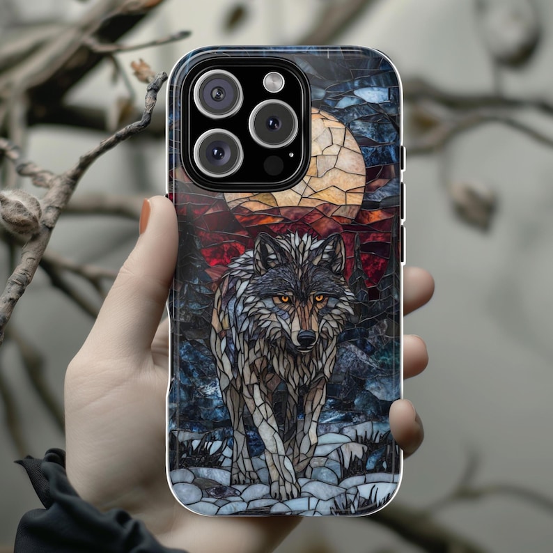 May include: A phone case featuring a mosaic-style image of a wolf under a full moon. The artwork uses shades of gray, blue, red, and yellow. The wolf is the central focus, with the moon and forest in the background.