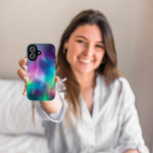 Puede incluir: Una funda para tel&eacute;fono con un dise&ntilde;o de aurora boreal colorido. La funda es negra y tiene una parte posterior transparente para mostrar el dise&ntilde;o. La funda est&aacute; siendo sostenida por una persona.