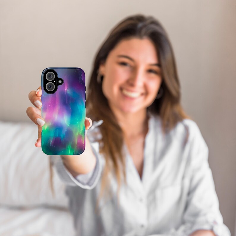 Puede incluir: Una funda para tel&eacute;fono con un dise&ntilde;o de aurora boreal colorido. La funda es negra y tiene una parte posterior transparente para mostrar el dise&ntilde;o. La funda est&aacute; siendo sostenida por una persona.