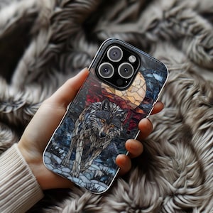 May include: A phone case featuring a wolf design. The artwork depicts a wolf under a full moon, with a stained-glass effect. The color palette includes shades of gray, blue, red, and yellow. The case is held in a hand, with a blurred background.