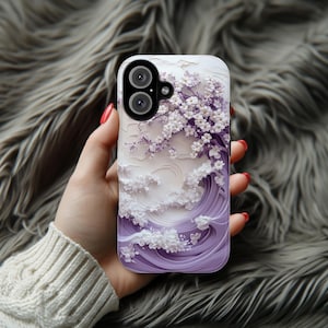 May include: A purple and white phone case with a 3D paper flower design. The flowers are white and the background is a purple wave pattern.