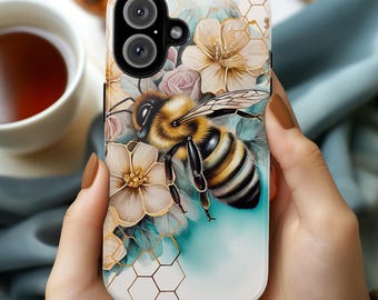 May include: A white phone case with a honeycomb pattern and a bee illustration. The bee is yellow and black with brown eyes and is surrounded by flowers. The flowers are white, pink, and blue.
