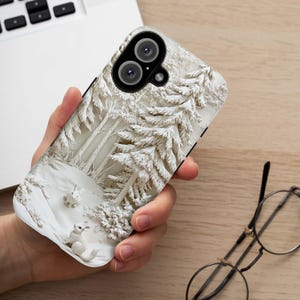 May include: A white phone case featuring a 3D design of a snowy forest scene. The case depicts two white rabbits in the foreground against a textured, white background.