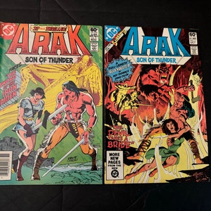 May include: Two comic book covers featuring the character Arak, Son of Thunder. The first cover is green and features Arak with a woman in a blue dress. The second cover is black and features Arak with a woman in a green dress. Both covers feature the title "Arak, Son of Thunder".