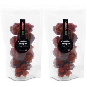 May include: Two clear plastic bags filled with dried Carolina Reaper chilies. Each bag has a black label with white text that reads "CALI PEPPER," "Carolina Reaper," and "Dried Chilies." The label also states the count of 15 peppers and "Extremely Hot."