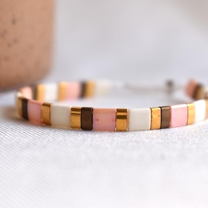 Könnte beinhalten: Ein Armband aus rosa, weißen, goldenen und braunen Perlen mit einem verschiebbaren Knotenverschluss.