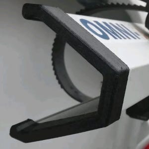 Op de afbeelding: Een wit mechanisch grijphulpmiddel met een zwart V-vormig opzetstuk. De witte behuizing toont de blauwe tekst OMNI. De zwarte bek heeft een getextureerd oppervlak en is gemonteerd aan de voorzijde van het apparaat, dat een cirkelvormig tandwiel bevat.