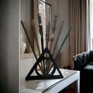 May include: A black triangular stand with a circle design, holding seven wooden wands. The stand is on a white table.