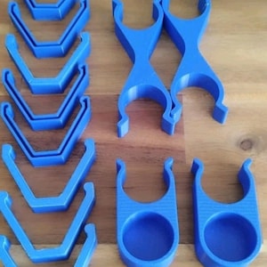 以下が含まれることがあります： 青いプラスチック製のクリップとホルダーのコレクション。画像には、いくつかのV字型のクリップ、2つの十字型のクリップ、および円形のベースを持つ2つのホルダーが表示されています。アイテムは木製の表面に配置されています。