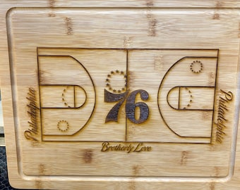 May include: A wooden cutting board with a basketball court design and the number 76 engraved on it. The words "Philadelphia" and "Brotherly Love" are also engraved on the board.