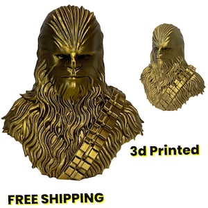 May include: A metallic gold-colored 3D printed bust of a Wookiee character featuring detailed fur texture and a bandolier strap across the chest. The sculpture displays a stern facial expression with visible eyes, nose, and mouth details.