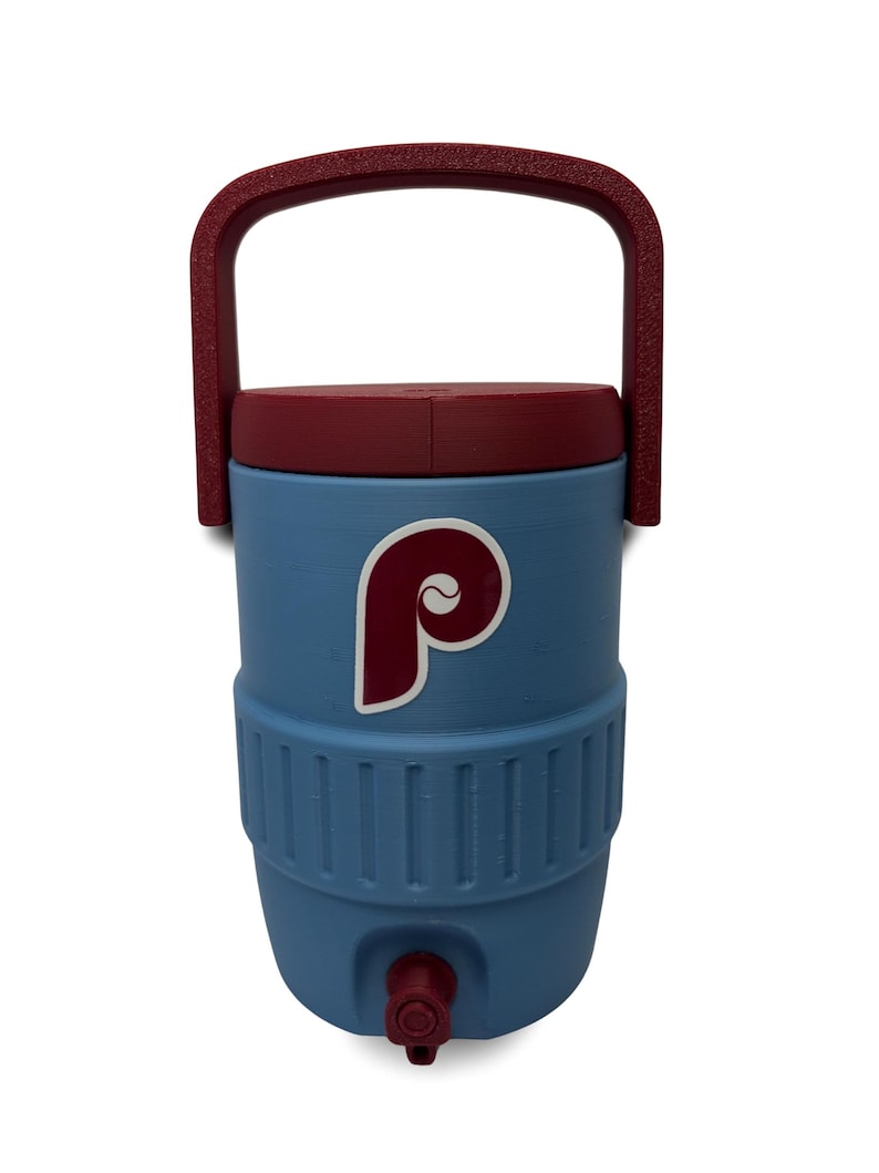 May include: A light blue beverage cooler featuring a maroon lid and a matching maroon handle. The front of the cooler displays a maroon and white letter P logo. A small maroon spigot is located at the bottom center of the cylindrical container.