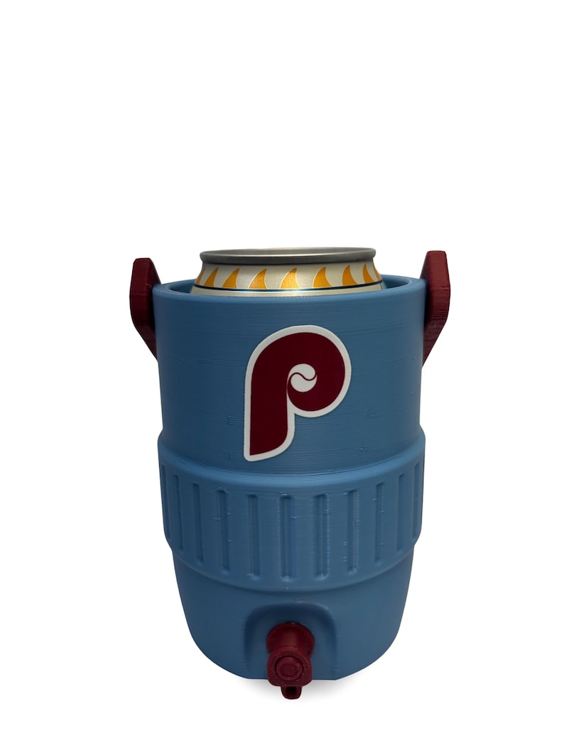 May include: A light blue beverage cooler shaped like a miniature water jug, featuring a maroon and white letter P logo on the front. The cooler has two maroon side handles, a maroon spigot at the base, and holds a silver aluminum beverage can.