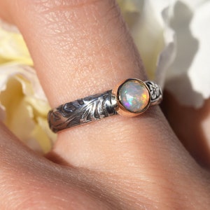 May include: A silver ring with an opal gemstone set in a gold bezel. The ring has a floral design.