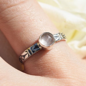 May include: A silver ring with a delicate floral design and a clear, faceted, pink gemstone.