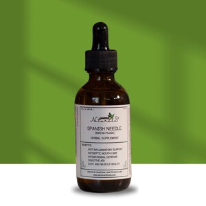 May include: A brown glass bottle with a black dropper, labeled "Spanish Needle" herbal supplement. The label lists benefits including anti-inflammatory support and antimicrobial defense. The bottle contains 2 fl oz (60 mL).